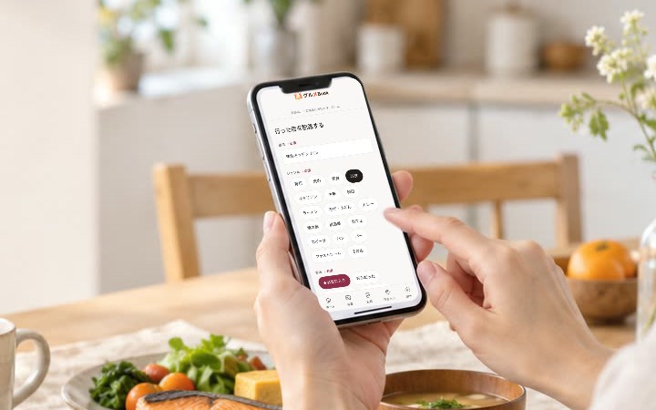 朝の食卓で、グルメBookの記録画面を開いたスマートフォンを手にしている人
